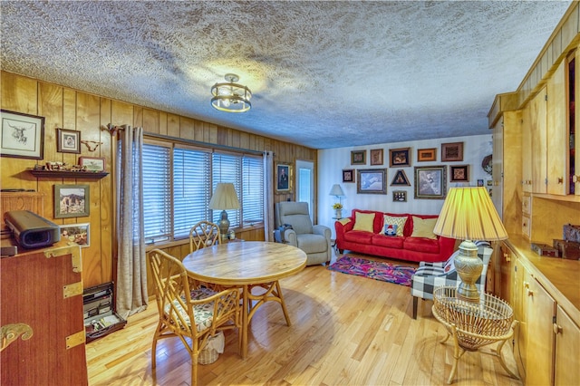 dining room with light hardwood / wood-style flooring, wood walls, and a textured ceiling