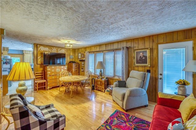 living room featuring wood walls, a wealth of natural light, a textured ceiling, and light hardwood / wood-style floors