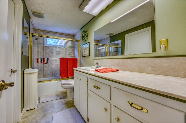 full bathroom with a textured ceiling, shower / bath combination with glass door, vanity, tile patterned floors, and toilet