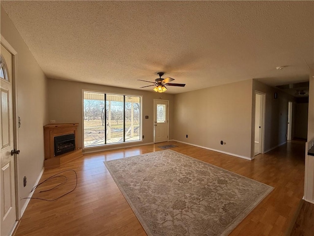 unfurnished living room with baseboards, ceiling fan, wood finished floors, a textured ceiling, and a fireplace