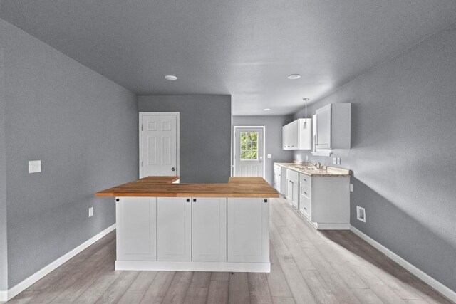 kitchen featuring butcher block counters, sink, light hardwood / wood-style flooring, and white cabinets