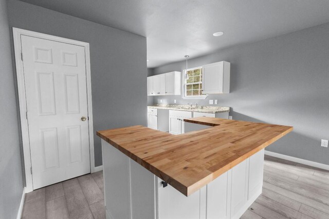 kitchen with sink, light wood-type flooring, white cabinets, a kitchen island, and wooden counters