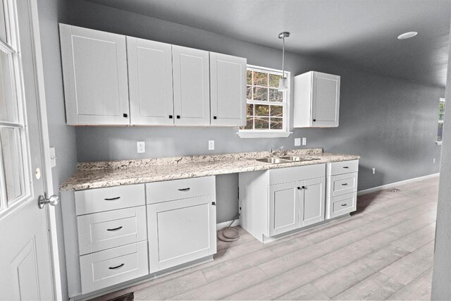 kitchen with hanging light fixtures, white cabinets, light hardwood / wood-style floors, light stone countertops, and sink