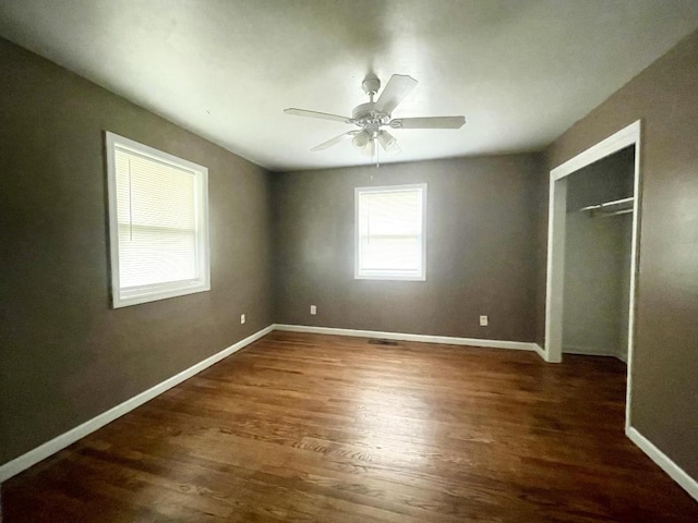 unfurnished bedroom with dark wood-type flooring, ceiling fan, a closet, and multiple windows