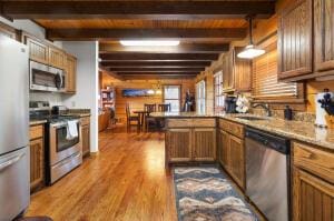 kitchen with a peninsula, appliances with stainless steel finishes, a sink, and beam ceiling