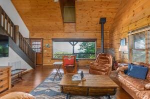 living room featuring a wood stove, wood walls, high vaulted ceiling, and wood finished floors