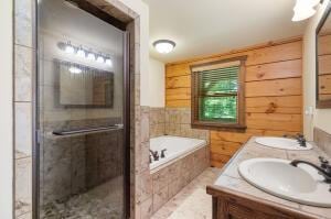 bathroom with a garden tub, double vanity, a stall shower, a sink, and wood walls