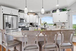 kitchen with a breakfast bar, stainless steel appliances, hanging light fixtures, and white cabinets