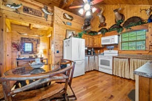 kitchen featuring ceiling fan, white appliances, wooden walls, and light hardwood / wood-style flooring