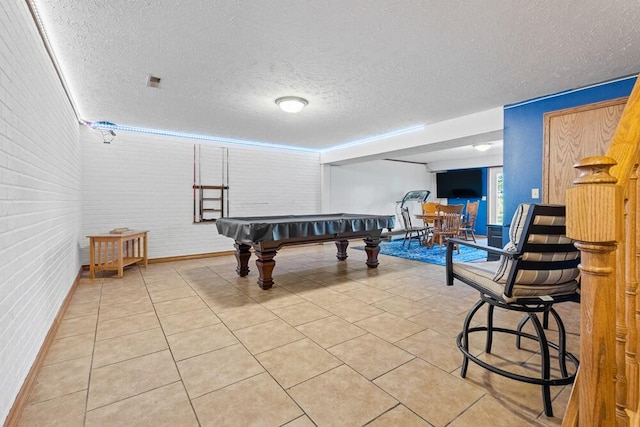 recreation room featuring light tile patterned floors, brick wall, a textured ceiling, and billiards