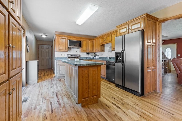 kitchen featuring light hardwood / wood-style floors, dark stone countertops, a textured ceiling, a center island, and stainless steel appliances