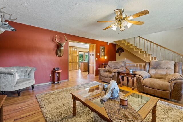 living room featuring wood finished floors, ceiling fan, stairway, and a textured ceiling