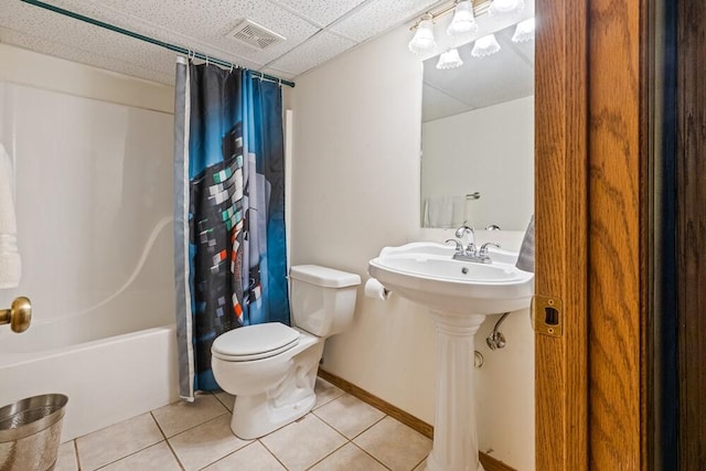 bathroom with a drop ceiling, shower / bath combination with curtain, toilet, and tile patterned floors