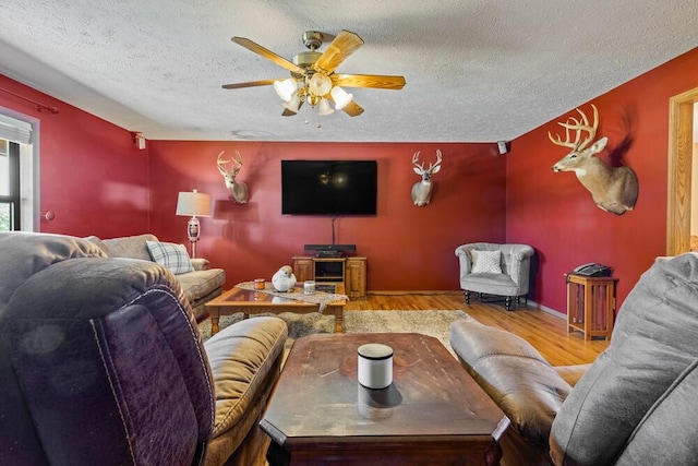 living room with ceiling fan, light wood-type flooring, and a textured ceiling