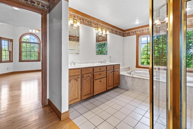 bathroom featuring tiled tub, vanity, ornamental molding, wood-type flooring, and a textured ceiling