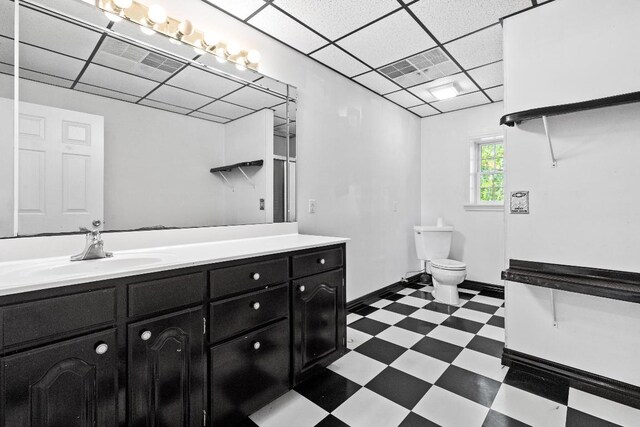 bathroom with a drop ceiling, toilet, tile patterned floors, and vanity