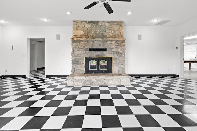 unfurnished living room with ceiling fan, a stone fireplace, and dark tile patterned floors