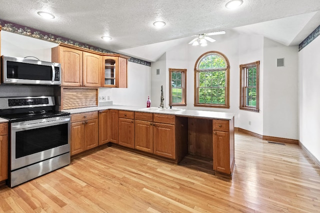 kitchen featuring appliances with stainless steel finishes, light hardwood / wood-style flooring, vaulted ceiling, and kitchen peninsula