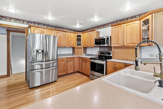 kitchen featuring light wood-type flooring, sink, stainless steel appliances, and a textured ceiling