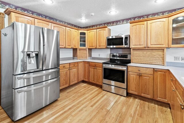 kitchen featuring a textured ceiling, stainless steel appliances, and light hardwood / wood-style floors