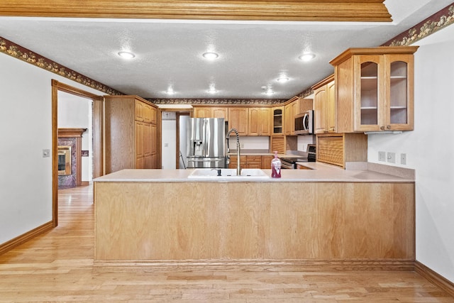 kitchen with appliances with stainless steel finishes, light hardwood / wood-style floors, sink, kitchen peninsula, and a textured ceiling