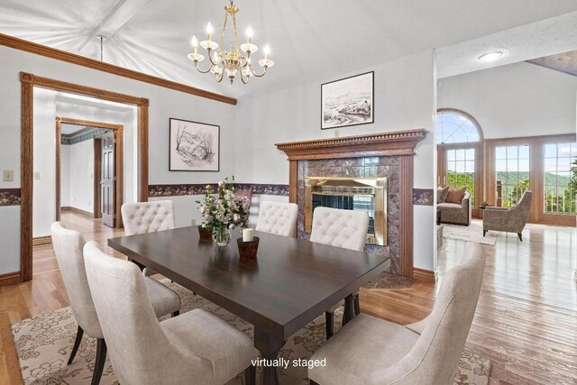 dining area with a fireplace, light hardwood / wood-style flooring, a notable chandelier, and vaulted ceiling