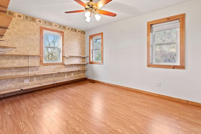 unfurnished room with ceiling fan, a textured ceiling, and light wood-type flooring