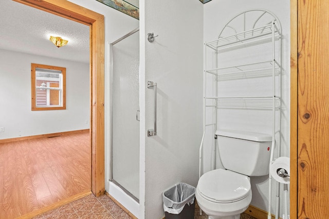 bathroom with a textured ceiling, hardwood / wood-style flooring, a shower with shower door, and toilet