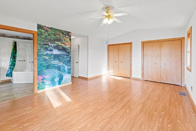 unfurnished bedroom featuring two closets, vaulted ceiling, ceiling fan, and light hardwood / wood-style flooring