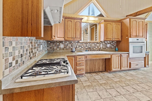 kitchen featuring sink, backsplash, oven, stainless steel gas stovetop, and vaulted ceiling