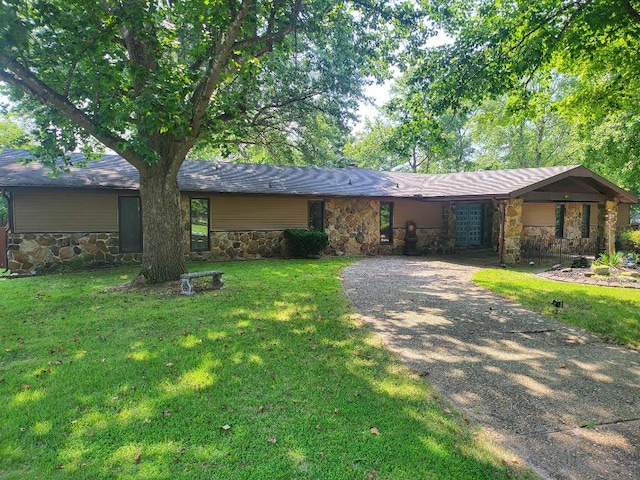 mid-century modern home with gravel driveway, stone siding, and a front lawn