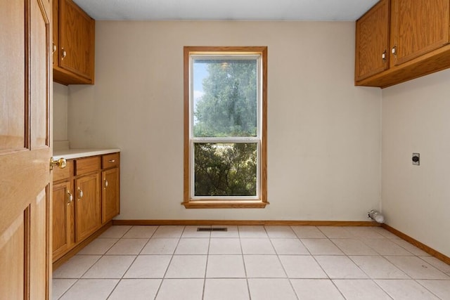 clothes washing area with light tile patterned floors, a wealth of natural light, electric dryer hookup, and cabinets