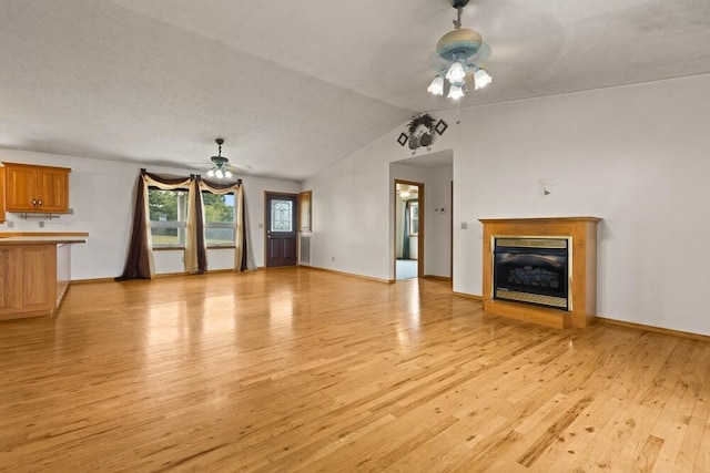 unfurnished living room featuring a textured ceiling, ceiling fan, light wood-type flooring, and lofted ceiling