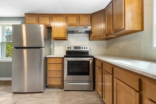 kitchen with light stone counters, light hardwood / wood-style flooring, decorative backsplash, and appliances with stainless steel finishes