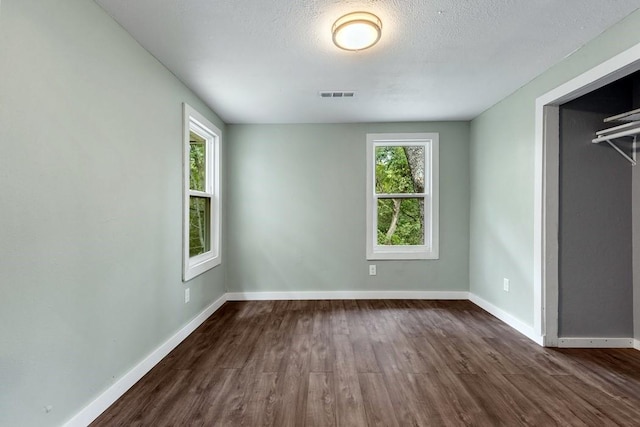 unfurnished bedroom featuring a closet, dark hardwood / wood-style floors, a textured ceiling, and multiple windows