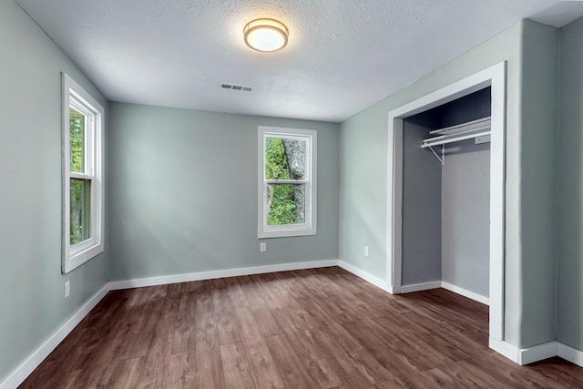 unfurnished bedroom featuring a closet, dark hardwood / wood-style floors, a textured ceiling, and multiple windows