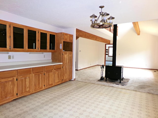 kitchen featuring hanging light fixtures, lofted ceiling with beams, a wood stove, a chandelier, and light carpet