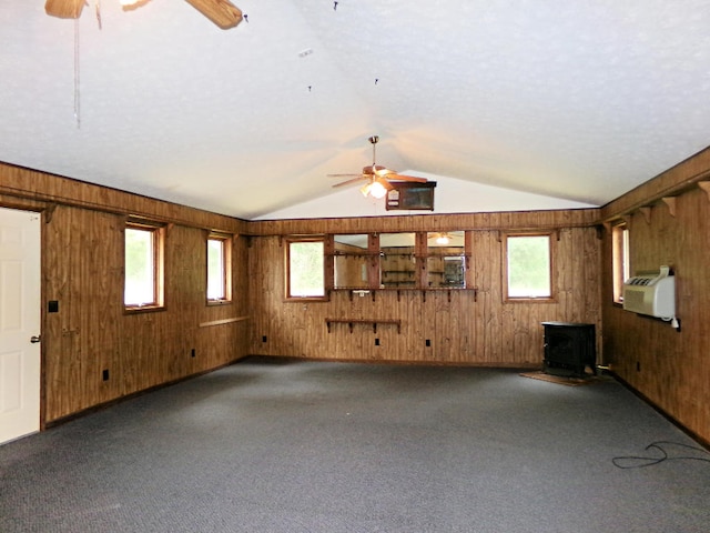 unfurnished living room featuring carpet flooring, a wood stove, ceiling fan, and wooden walls