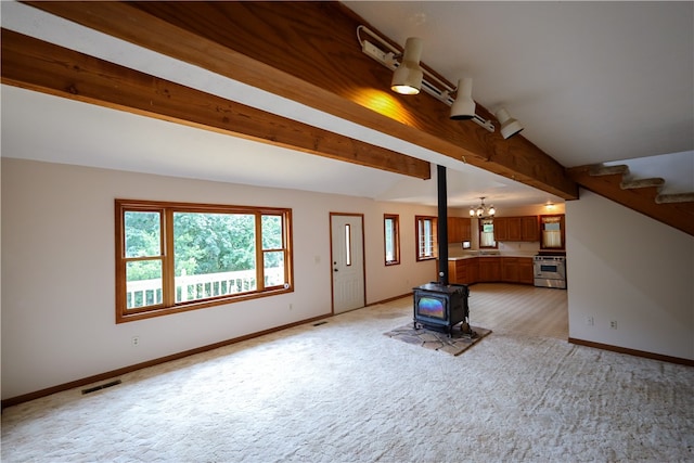 unfurnished living room with a wood stove, an inviting chandelier, light carpet, and vaulted ceiling with beams