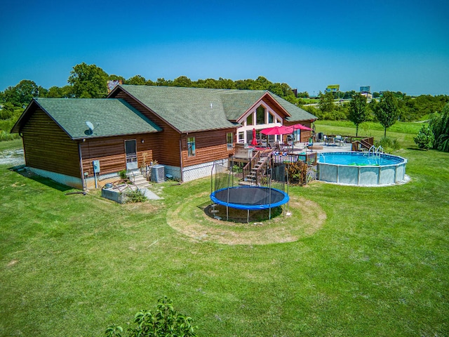 back of property with a swimming pool side deck, cooling unit, a trampoline, and a yard