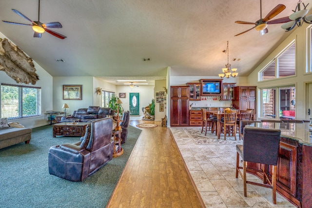 living room with a textured ceiling, light hardwood / wood-style flooring, high vaulted ceiling, and ceiling fan with notable chandelier