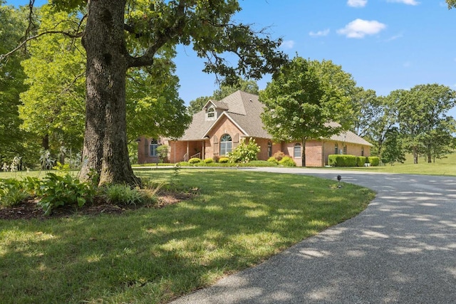 view of front of house featuring driveway, brick siding, and a front yard