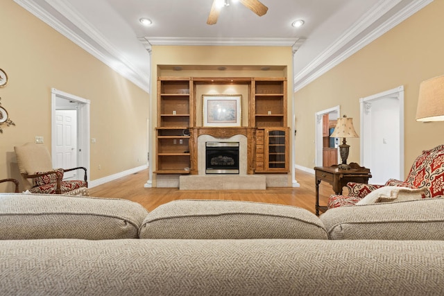 living room with a fireplace with raised hearth, ornamental molding, light wood finished floors, and built in shelves