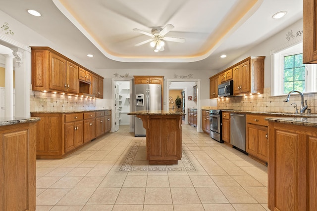 kitchen with decorative backsplash, a tray ceiling, stainless steel appliances, sink, and light stone counters