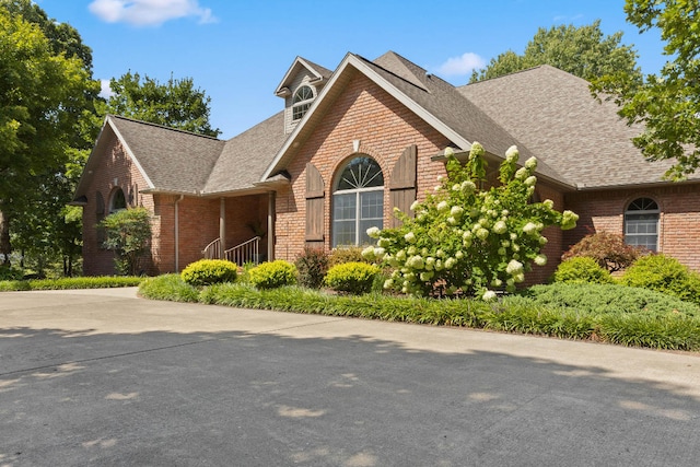 view of front of house featuring roof with shingles, concrete driveway, and brick siding