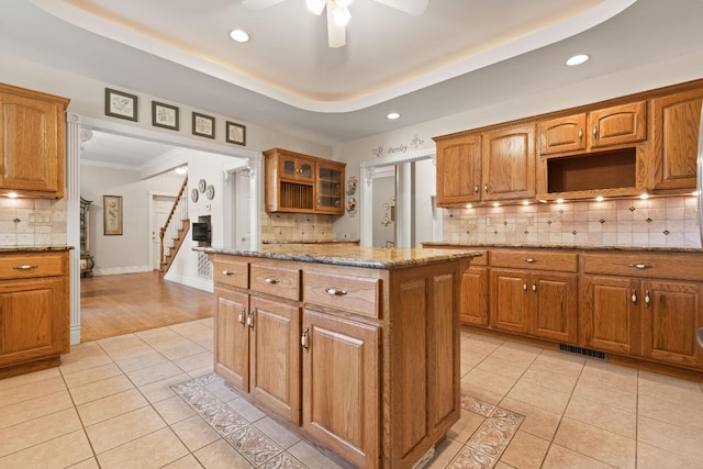 kitchen with visible vents, a kitchen island, brown cabinets, light stone countertops, and light tile patterned flooring