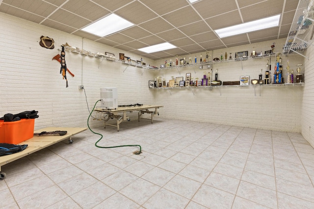 miscellaneous room with a drop ceiling and brick wall