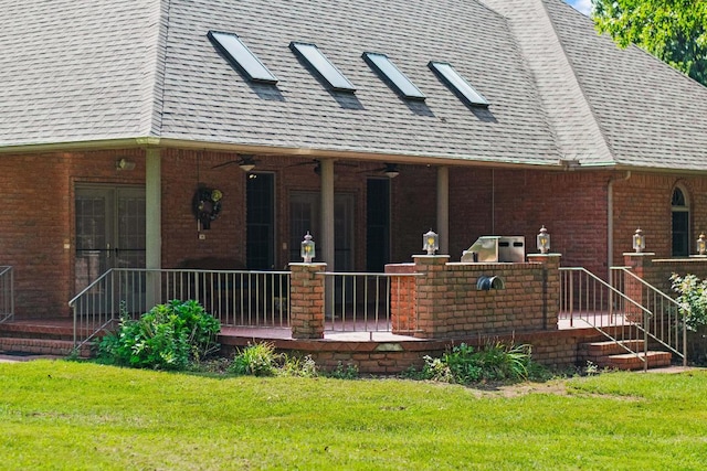 rear view of property featuring a ceiling fan, brick siding, a lawn, and roof with shingles