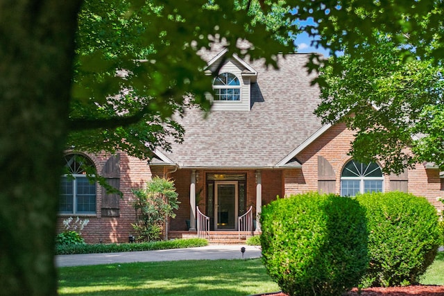 view of front of home with a shingled roof, a front yard, and brick siding