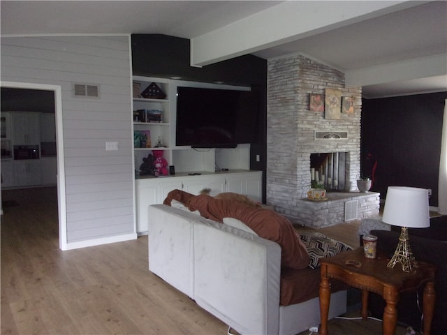 living room with built in shelves, light hardwood / wood-style flooring, a stone fireplace, and lofted ceiling with beams